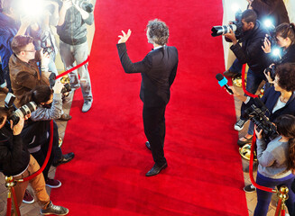 Celebrity arriving at red carpet event waving at photographing paparazzi