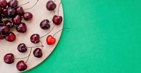 Sweet cherry on a wooden cutting board on a green background.One bright red heart-shaped...