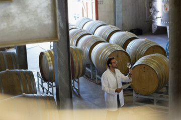 Vintner in lab coat examining wine in winery cellar
