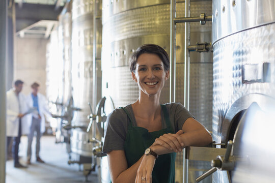 Portrait smiling vintner at stainless steel vat in winery cellar