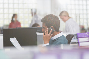 Businessman with paperwork talking on cell phone in office