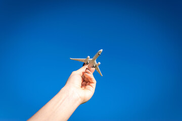 Plane banner. Toy airplane flight in air, travel concept. Aircraft fly in sunlight blue sky in pilot hand on bright sun light background.