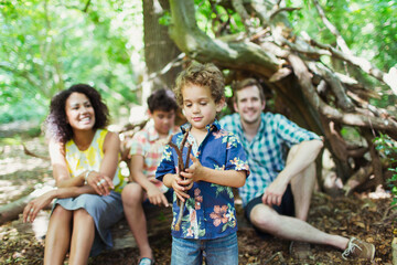Family watching boy play with sticks in woods