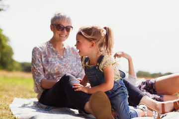 Grandmother and granddaughter laughing on blanket in sunny field