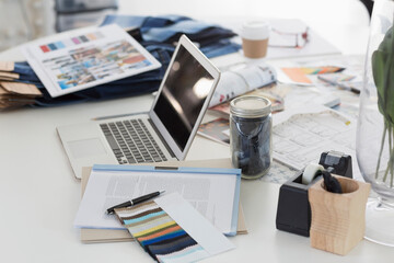 Laptop, swatches, proofs and paperwork on desk in fashion desk office