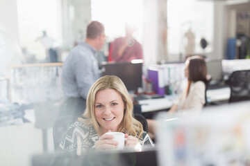 Portrait smiling fashion designer drinking coffee at computer in office