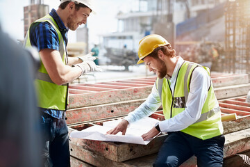 Construction worker engineer reviewing blueprints at construction site - obrazy, fototapety, plakaty