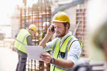 Engineer digital tablet talking on cell phone at construction site - obrazy, fototapety, plakaty