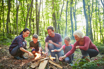 Multi-generation family roasting marshmallows at campfire in forest
