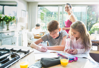 Mother watching brother and sister doing homework at kitchen counter