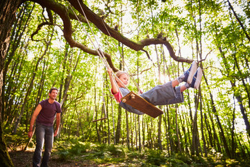 Father pushing daughter on rope swing in forest