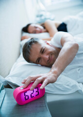 Man in bed turning off morning alarm clock