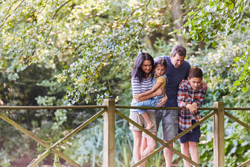 Naklejka na ściany i meble Family standing on footbridge in park with trees
