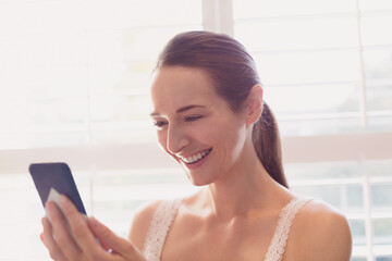 Smiling woman texting with cell phone at window