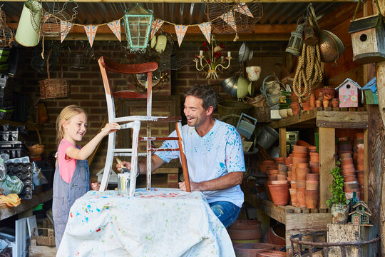 Father and daughter painting chair in workshop