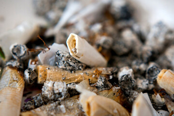 Closeup of old cigarette butts lying in a full ashtray.