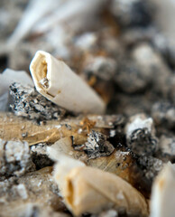 Closeup of old cigarette butts lying in a full ashtray.