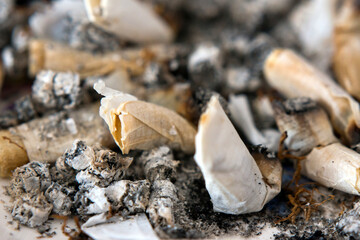 Closeup of old cigarette butts lying in a full ashtray.