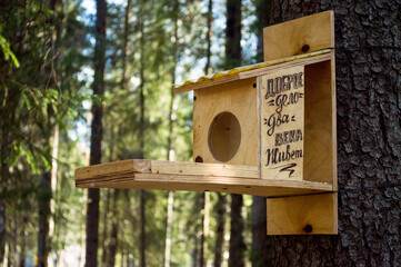 YA yellow-green wooden bird feeder and squirrel is tied to a tree trunk. There is an inscription on the mangers