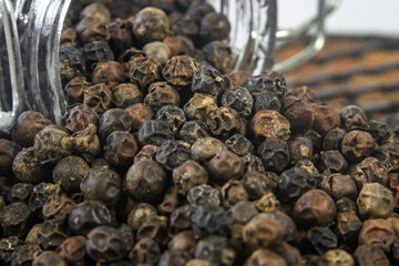 Dried black pepper seeds from glass jar on wooden table close up