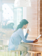 Woman drinking coffee and using digital tablet at breakfast bar