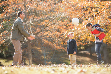 Father and sons playing soccer in autumn park