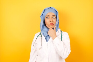 Oops! Young beautiful doctor muslim woman wearing a medical uniform and hiyab over yellow isolated background Thinking worried about a question, concerned and nervous with hand on chin.