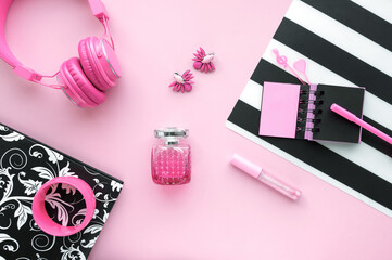 Fashion female flat lay on pink, black and white striped background with pink women accessories - perfume,headphones,earrings,notepad,pen,bracelet and lip gloss. Beauty, pink color,minimalism concept.