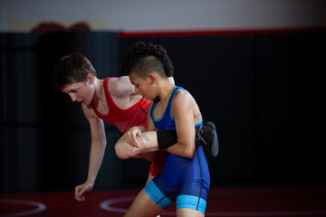 Wrestlers in red and blue singlets practicing on a red mat. 