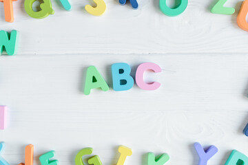 Close up Multicolored wooden letters with ABC on white wooden background. Set of toys for studying alphabet. Education, back to school concept. Top view, copy space