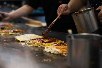 Hand spreading an Okonomiyaki sweet savory sauce at the top. Making a Hiroshima Japanese style...