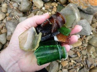 Hand of a woman holding broken glass from a rocky beach clean up