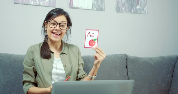 Young woman teacher showing pictures with the alphabet, learning letters and words, studying with a child or kids online using a laptop at home. Preschool Online Education Concept