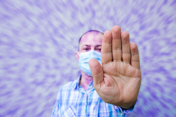 Man wearing a surgical face mask and making the hand gesture to stop