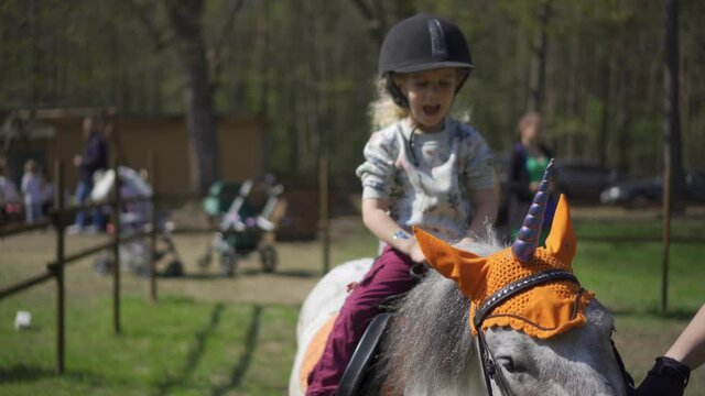 Artificial unicorn pony and adorable girl child with helmet ride it. Gimbal shot