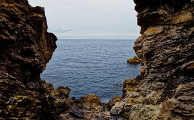 Looking out over a calm sea from within a rough crevice on an overcast day