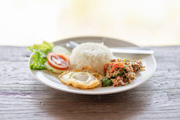 Rice topped with stir-fried pork with basil and fried egg on wooden table
