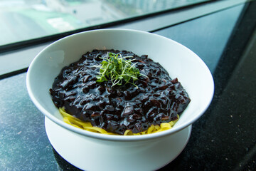 Korean-chinese traditional black bean noodles, Jajangmyeon, on a black table.