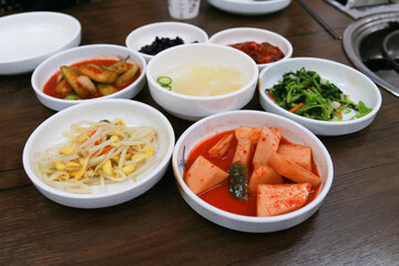 Korean traditional side dish radish, kimchi, bean sprouts, vegetables,seaweed, cucumber and soup on a wooden table.