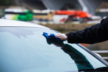 Hand cleaning a car’s windshield with a micro fiber cloth. Washing vehicle front windshield glass.