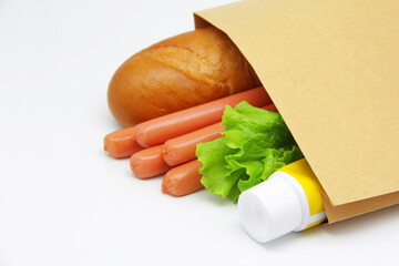 A set of fresh foods to make delicious, traditional hot dogs. Ingredients for a hot dog. Bread, sausage, salad, a tube of mustard in a Kraft bag on a white background. A copy of the space.