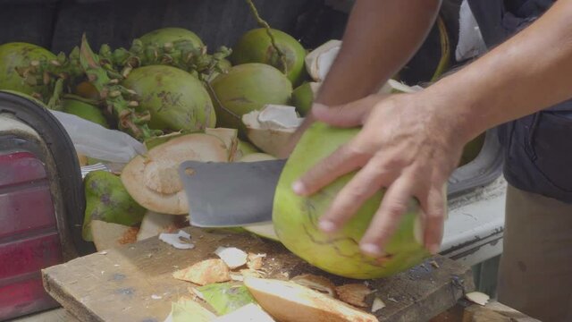 Green fresh coconut peeling and shelling with heavy chop knife for juice.