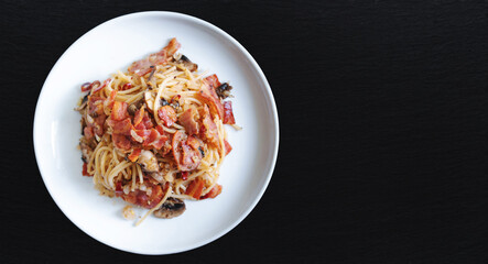 Stir fry Spaghetti bacon with Champion mushroom in white dish on black stone table top, with copy space