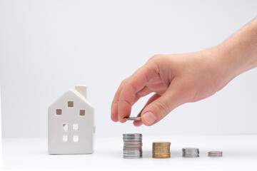 Concept of investment in property, hand putting coin with white house on background.