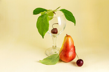 Abstract still life with wineglass, ripe cherries and pears on a light yellow background. Creative minimal background. Drinks concept.
