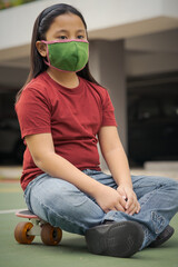 Young girl wearing mask sitting on a skateboard outdoor.