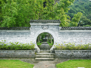 A Chinese style courtyard circular moon gate leads to an inner garden with green bamboos. The Chinese characters on the gate says 'Admiring Bamboo Garden'. County of Xincheng, Guangxi, China