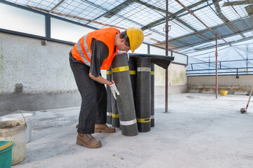 Waterproofing of a roof – floor. Man with rolls of bituminous waterproofing membrane. Sealing and...
