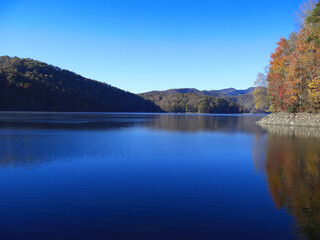 Scenic view of Nantahala Lake in the Smoky Mountains of North Carolina, USA. The coloured forest is reflecting in the water under a clear blue sky.