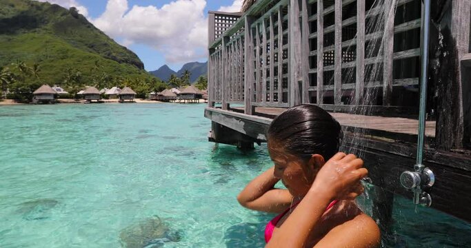 Travel luxury. Woman taking shower outside in bikini at resort hotel on travel at resort hotel overwater bungalow in Tahiti. Vacation in paradise. Multiracial girl showering after swimming in lagoon